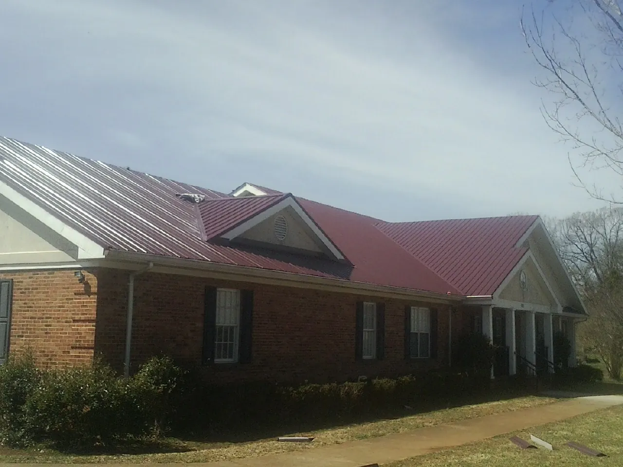 Red metal roof with gabled entries on a long brick building, from a Hail Damage Roof Repair job in Houston
